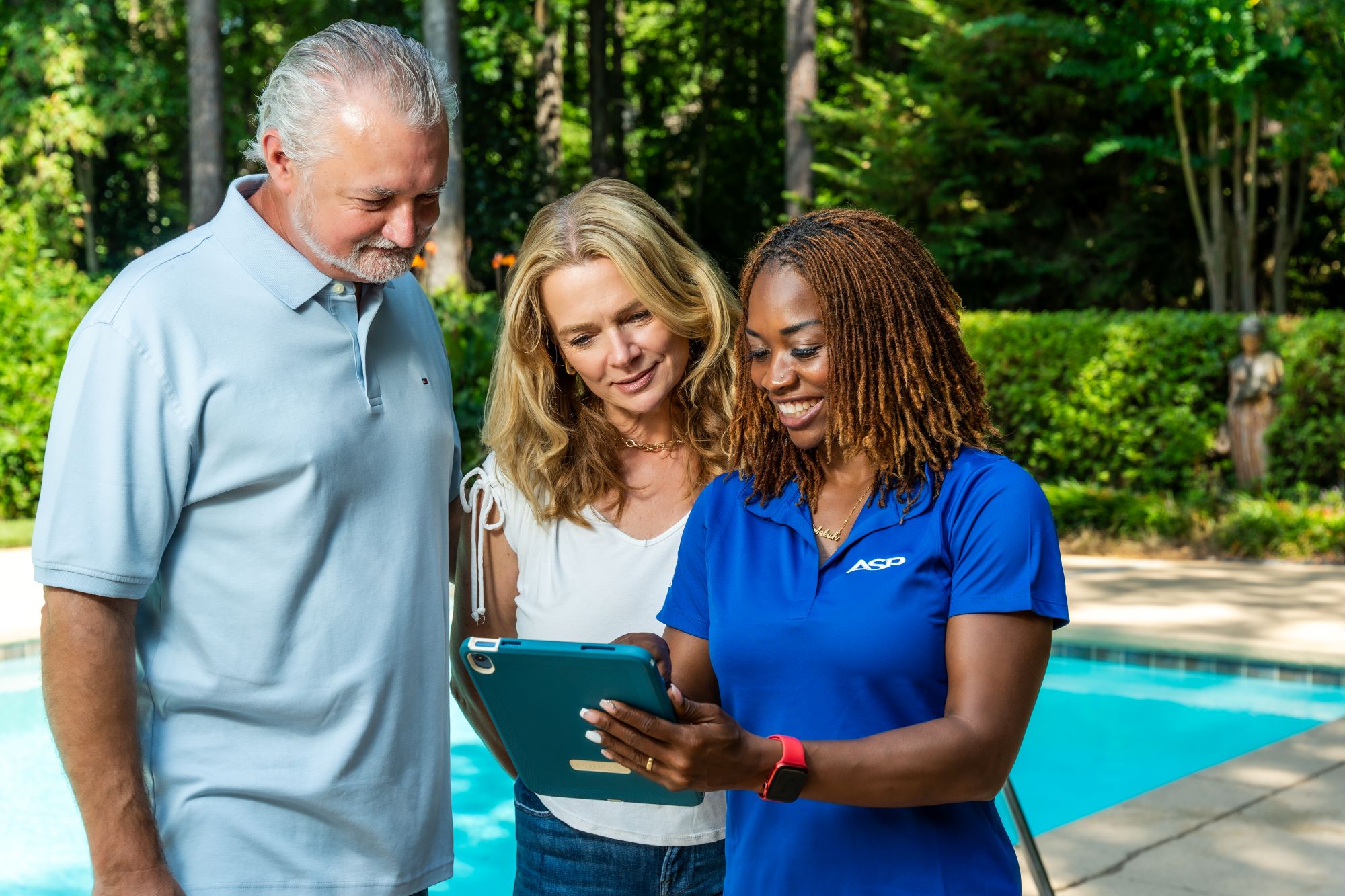 Female ASP franchise outdoor business owner meets with two homeowners in front of a pool.